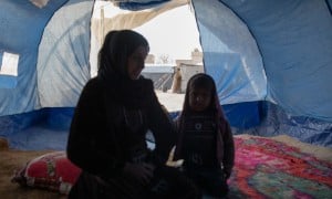 Woman and little girl sitting inside of a blue tent in Syria