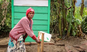 A woman in a pink sweater washing her hands at an outdoor tap in DRC