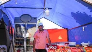 A man stands in the middle of his grocery shop, which is being housed in a temporary tent