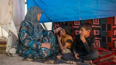 Shahinaz* and her grandsons sit in their tent at a camp  in north-west Syria following the 2023 earthquakes. Photo: Karam Al-Masri/Arete/DEC