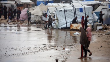 People in Gaza walk around a large pool of water that has flooded their campground
