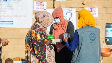 Three woman stand in front of a wall with UK Aid signs