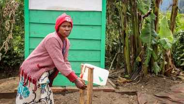 A woman in a pink sweater washing her hands at an outdoor tap in DRC