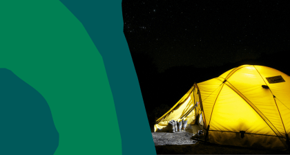 A glowing yellow tent illuminated from within stands in a dark campsite under a star-filled night sky. Hiking boots and trekking poles rest outside the entrance, suggesting a day of adventure.
