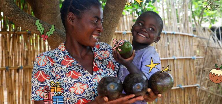 A smiling woman and young boy hold several large avocados under a tree, with Christmas-themed illustrations of stars, holly, presents, and pudding added around them for a festive touch.