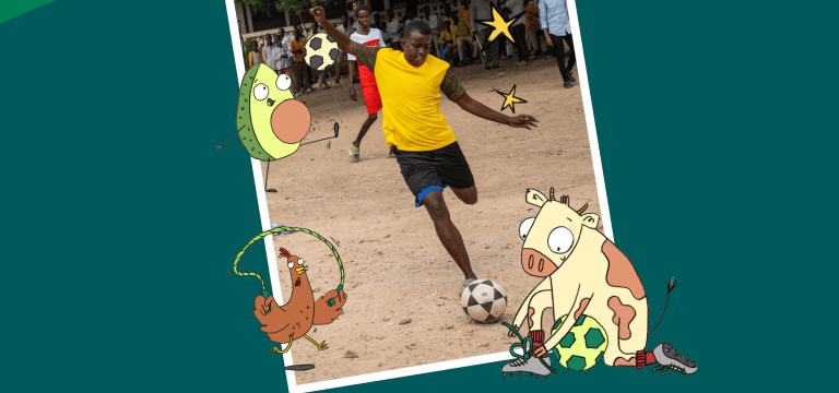 A football player wearing a bright yellow shirt and black shorts kicks a football on a dusty outdoor pitch. Spectators stand and watch from the sidelines beneath large trees in the background. The image captures an energetic moment during a community football match, with the player focused on striking the ball while others look on.