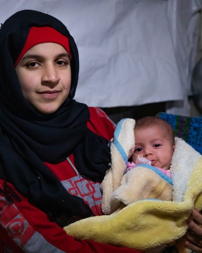 Wafdeh* (20) with her youngest daughter Rajaa* (2 months) with their thermal blanket in their makeshift kitchen. Photo: Gavin Douglas / Concern Worldwide.