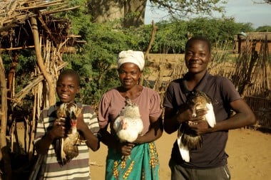 A smiling woman and two boys stand outdoors, each proudly holding a duck in their arms.
