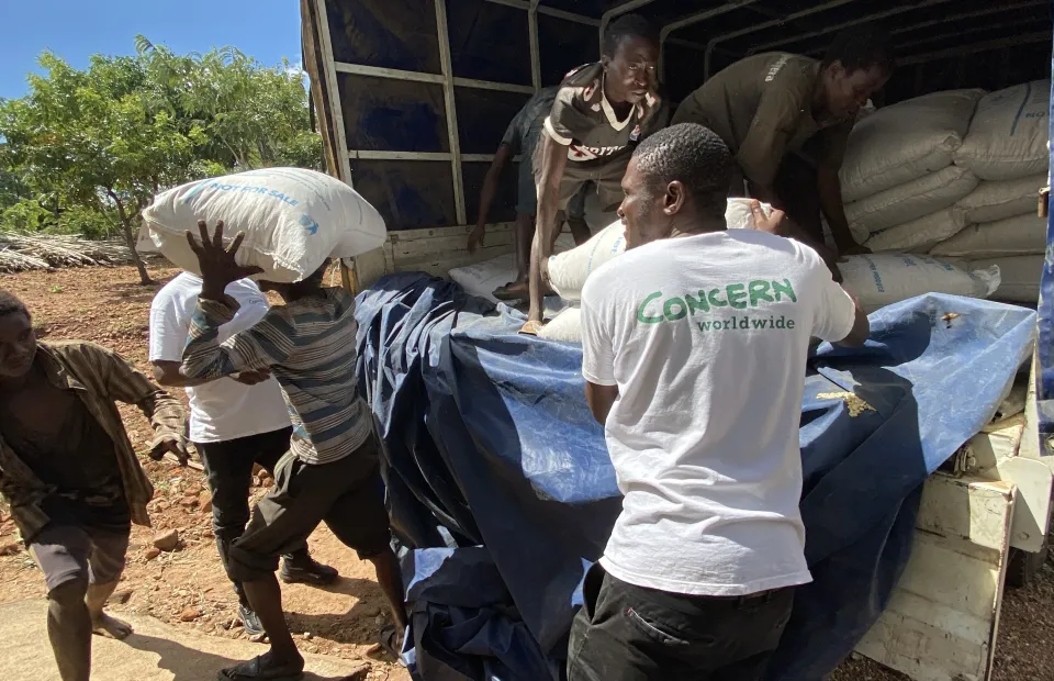Concern staff in white tshirts with the Concern Worldwide and community members, unload food supplies out of a truck.