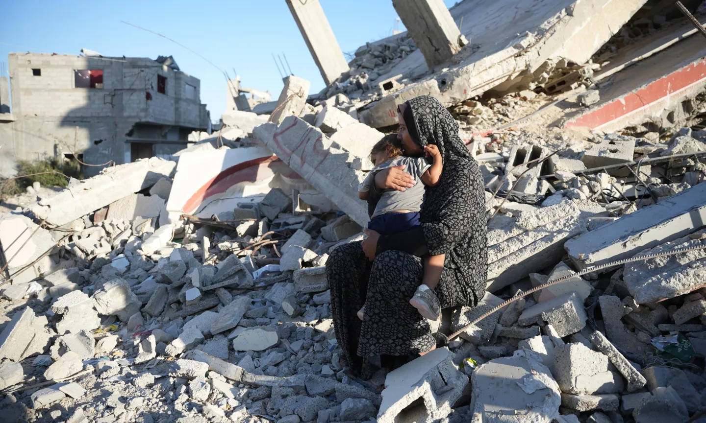 Aaliyah* holds her daughter on the remains of a damaged building in Gaza, October 2024. The mother of six built a temporary shelter opposite her demolished house and depends entirely on aid to feed her family. Photo: DEC/Arete/Abdallah Alsayed
