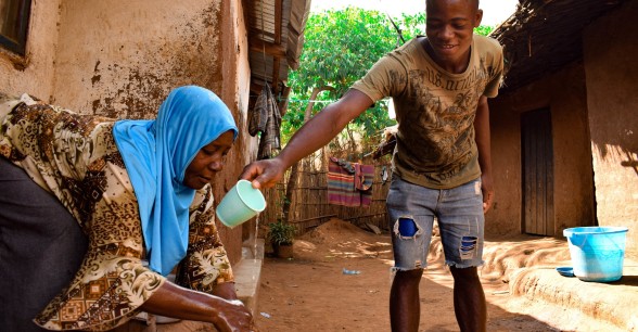 Marriam Jamali received soap as part of of hygiene distribution to help prevent the spread of Covid-19 by Concern in Lilongwe. Her son Bruno helps pour water on her hands while she washes them.