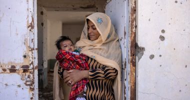 Nasima* (holds her son Rahmin* (2 months old) standing in the doorframe of what was once Sangin's clinic, bombed out and destroyed. There is currently no healthcare available. Photo: Stefanie Glinski