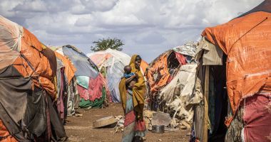 Somalian woman carrying child, surrounded by informal tents 