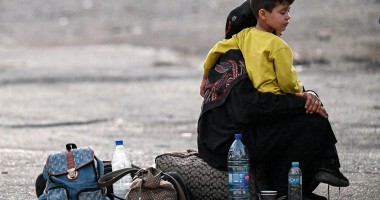 A woman sits with a child on her lap next to bags on the ground as people fleeing from Lebanon arrive on the Syrian side of the border with Lebanon in Jdeidat Yabus in southwestern Syria on September 24, 2024. (Photo: Louai Beshara/AFP via Getty Images)
