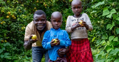 Father stands with two children on their farm, holding lemons