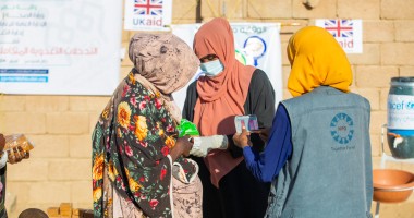 Three woman stand in front of a wall with UK Aid signs