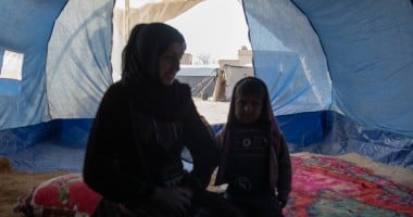 Woman and little girl sitting inside of a blue tent in Syria