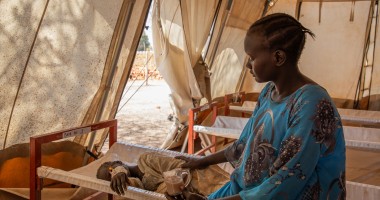 A mother in a blue dress sits with her child in a health clinic