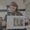 A young Scout wearing a green neckerchief and navy hoodie smiles at the camera while holding a Concern Worldwide educational activity sheet about Yemen. The sheet includes information about a family affected by malnutrition alongside a photograph of three children.