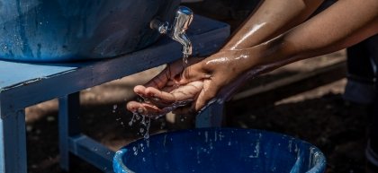 Trevor (4) washes his hands. Ambeza Idd, (35) (blue vest) mans the hand washing station. Kibera Slum, Nairobi, Kenya Photo: Ed Ram / Concern Worldwide