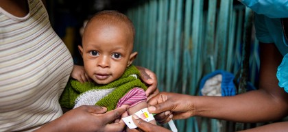 Jane holds her baby Mark (11 months) as a nurse uses a MUAC band to check his nutrition status. Photo: Ed Ram