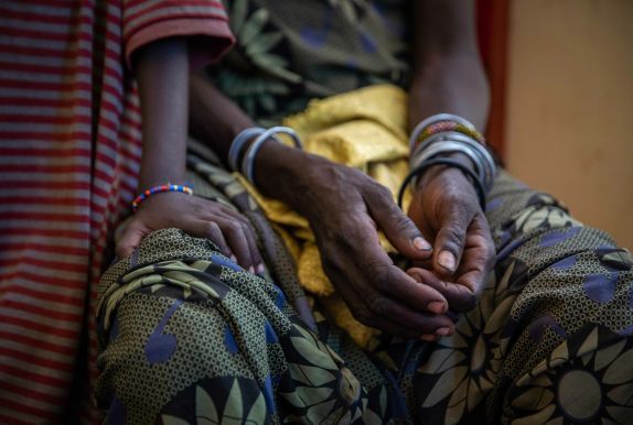 Close up of Kenyan woman's hands resting on her lap, with child's hand on her knee