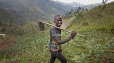 Gerard Ndabahekeye (28) with his new hoe bought with the profits of his business, a small shop, which he was able to set up due to the investment of the Graduation Programme. Photographed in his cassava field near his home in Bukinanyana, Cibitoke, Burundi. Photo: Abbie Trayler-Smith / Concern Worldwide