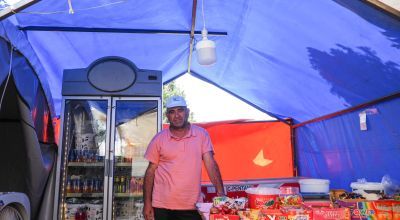 A man stands in the middle of his grocery shop, which is being housed in a temporary tent