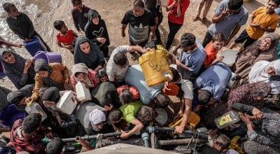 People gather with jerrycans and other containers to collect water from a tanker cistern in Deir el-Balah in the central Gaza Strip