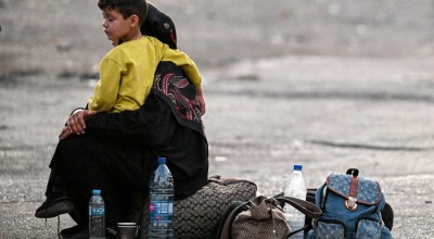 A woman sits with a child on her lap next to bags on the ground as people flee from Lebanon. Photo by LOUAI BESHARA/AFP via Getty Images