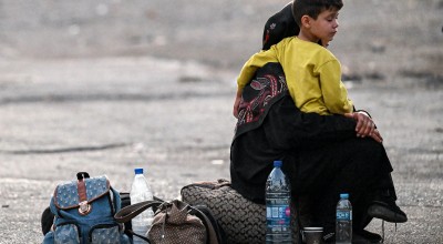 A woman sits with a child on her lap next to bags on the ground as people fleeing from Lebanon arrive on the Syrian side of the border with Lebanon in Jdeidat Yabus in southwestern Syria on September 24, 2024. (Photo: Louai Beshara/AFP via Getty Images)