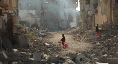 Child on tricycle cycles through destroyed buildings in Gaza