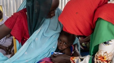 A mother holds her child as their temperature is taken but a healthcare professional at a health centre.
