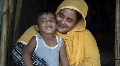A mother wearing yellow looks down smiling at her young son.