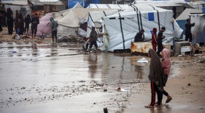 People in Gaza walk around a large pool of water that has flooded their campground