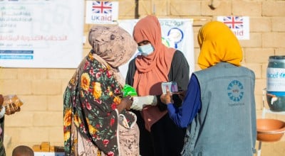 Three woman stand in front of a wall with UK Aid signs
