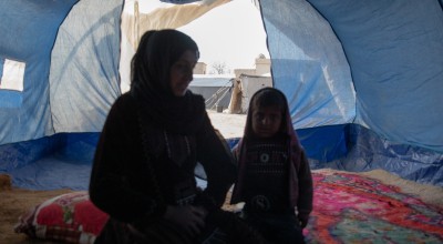 Woman and little girl sitting inside of a blue tent in Syria
