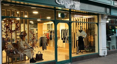 An image of a dark green shop front. Concern Worldwide's logo is above and the windows show a warm, well dressed window display of women's clothing.