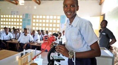 A young woman in a classroom standing beside a microscope.