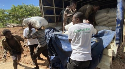 Concern staff in white tshirts with the Concern Worldwide and community members, unload food supplies out of a truck.