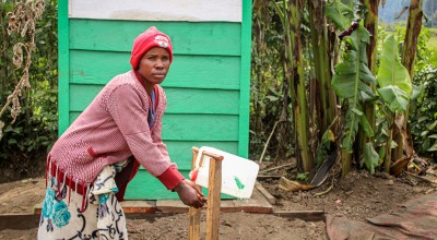 A woman in a pink sweater washing her hands at an outdoor tap in DRC