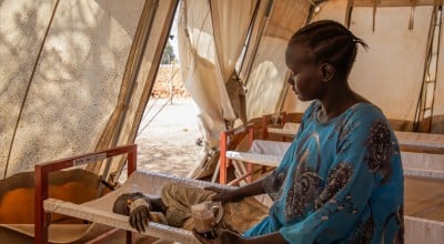 A mother in a blue dress sits with her child in a health clinic