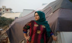 A woman in a green headscarf and pink dress stands in front of a tent.