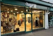 An image of a dark green shop front. Concern Worldwide's logo is above and the windows show a warm, well dressed window display of women's clothing.