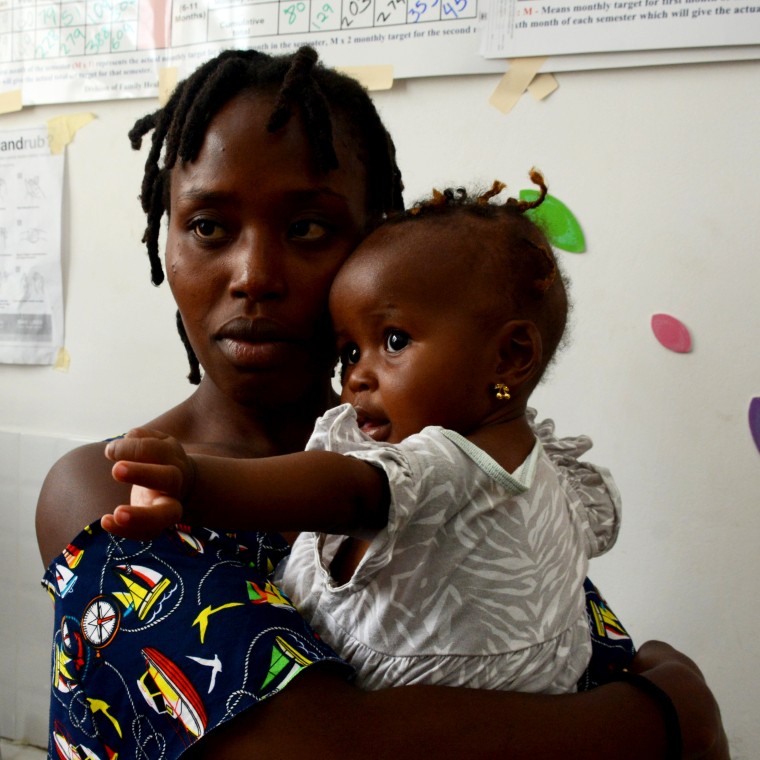 A mother in a patterend dress holds her baby dressed in white.