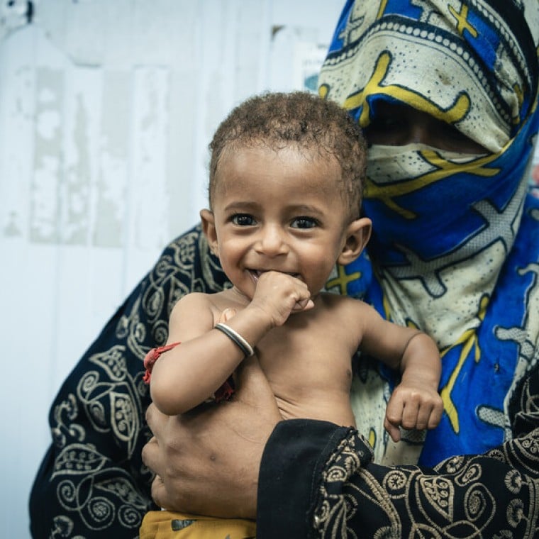 A seven month old smile smiles in his mother's arms.