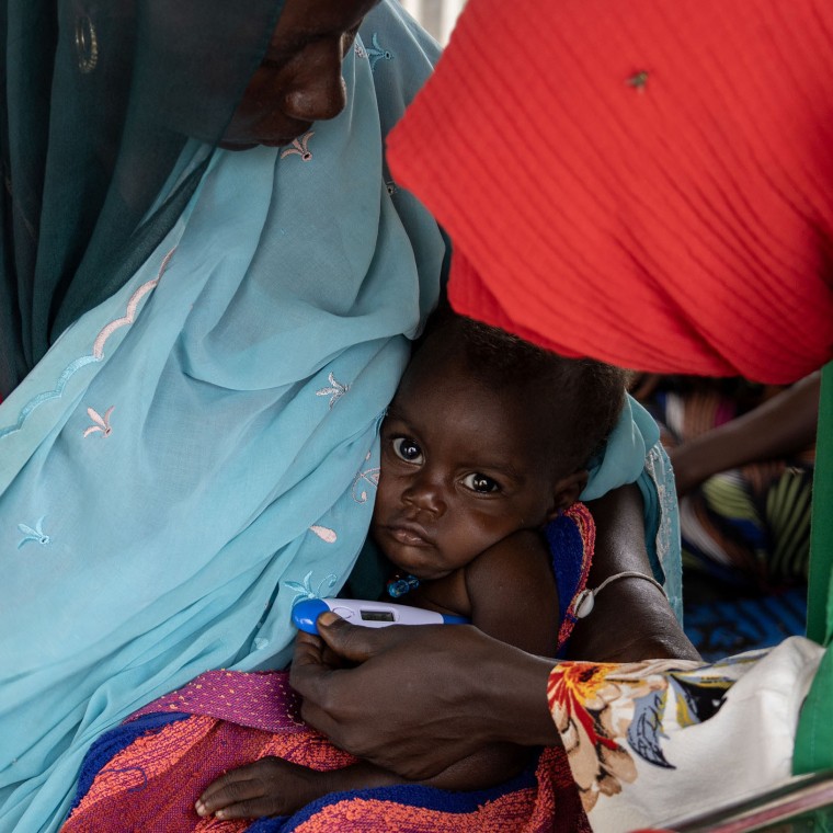 A mother holds her child as their temperature is taken but a healthcare professional at a health centre.
