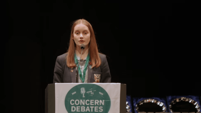 A young woman stands in school uniform at a podium that reads Concern Debates.